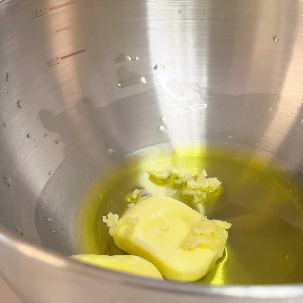 Ajo machacado añadido a la mezcla de aceite de oliva y mantequilla en el cuenco metálico.