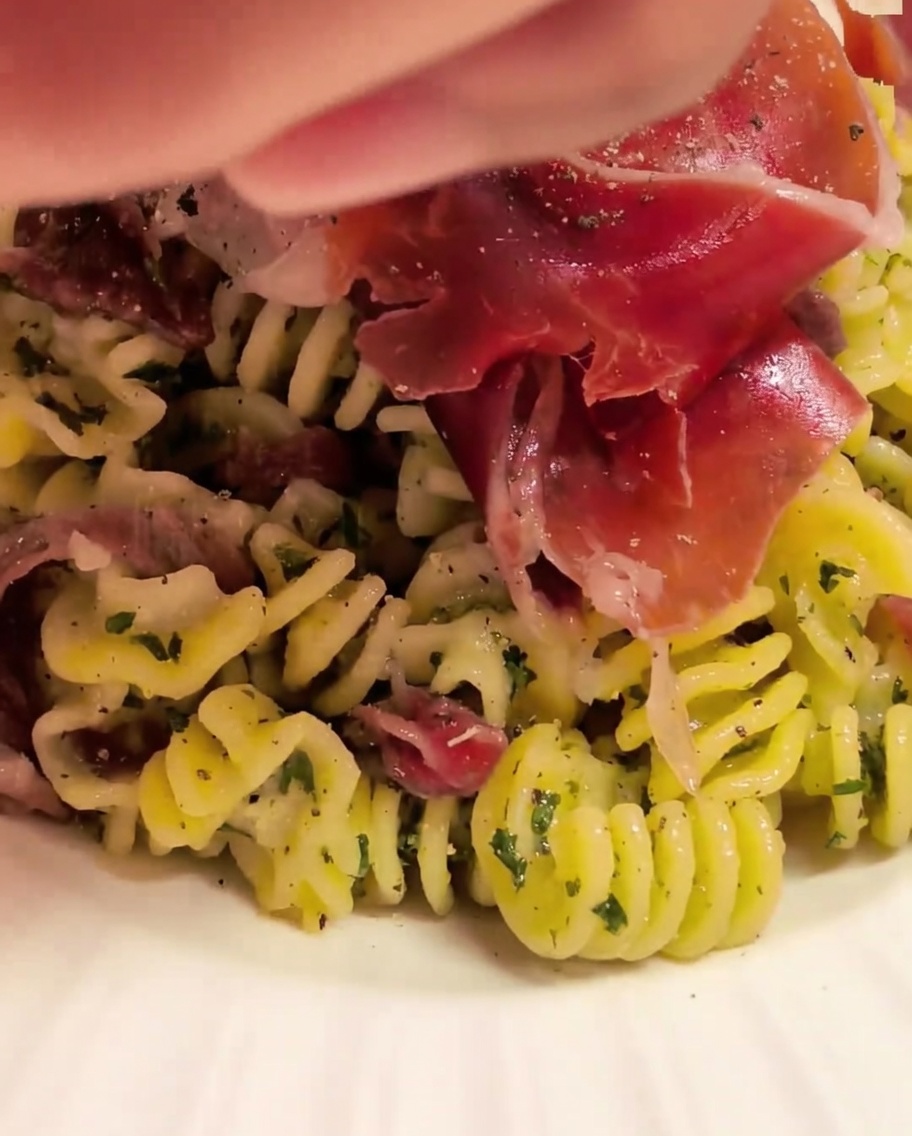 Pasta en espiral mezclándose en un cuenco con la salsa usando pinzas de cocina.