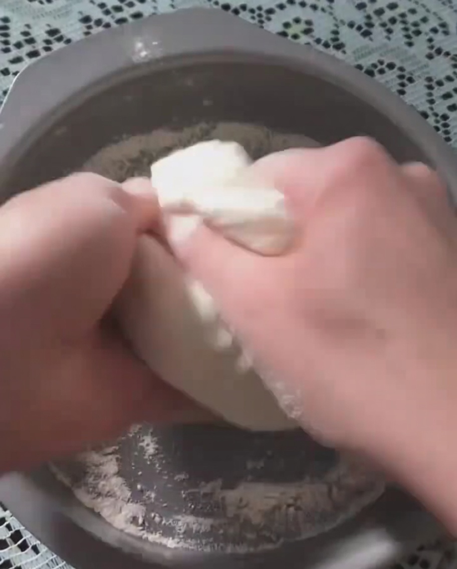 Manos presionando la masa de pizza fermentada en una bandeja de horno circular de metal.