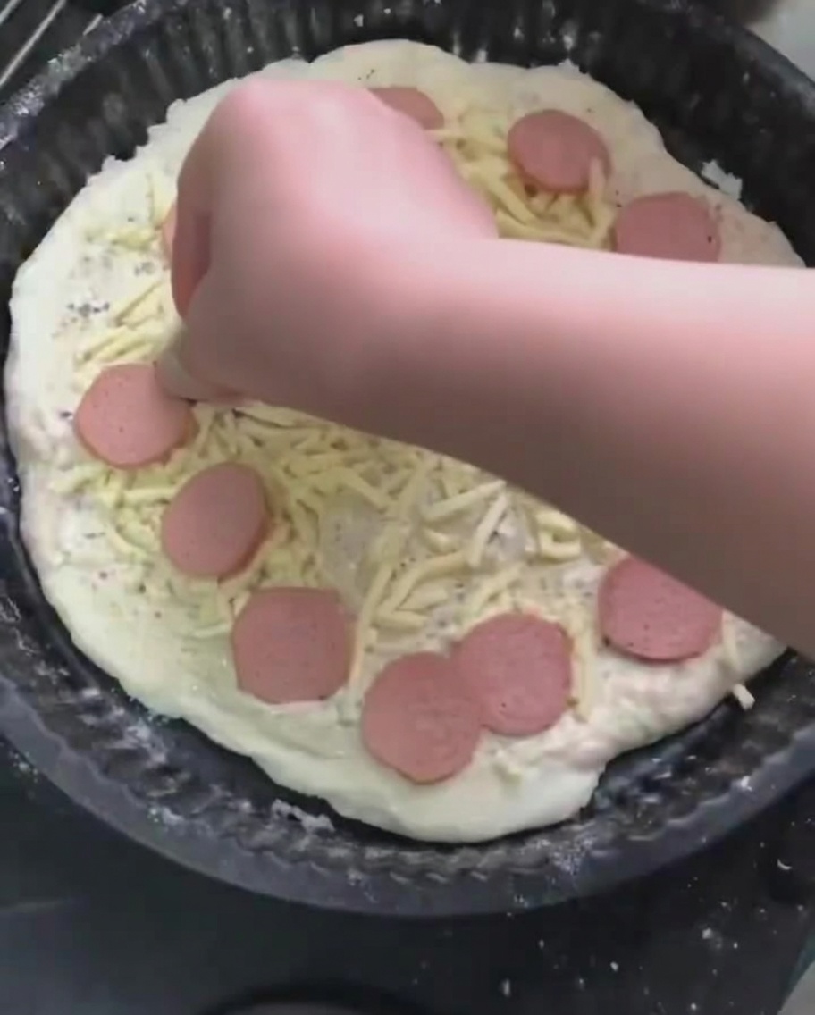 Rodajas de salchicha siendo colocadas sobre la cama de queso mozzarella rallado en la pizza.
