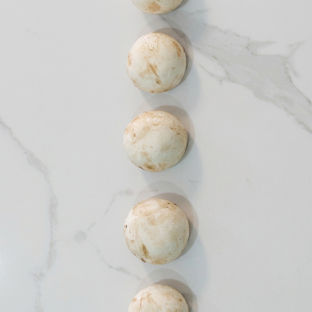 Rodajas de champiñones blancos salteándose en una sartén con crema hasta estar tiernos y dorados.