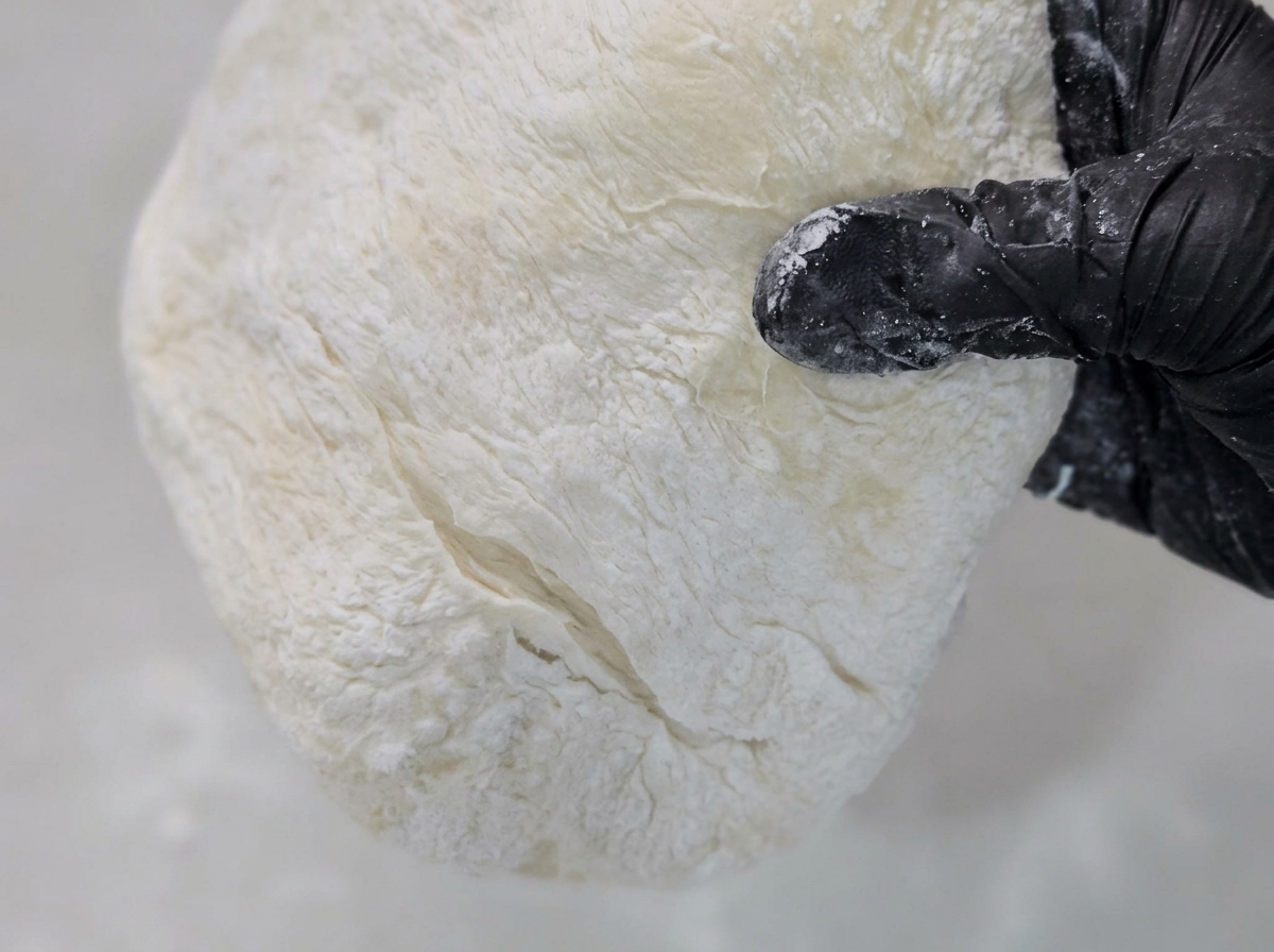 Masa de pizza siendo aplanada y estirada sobre una superficie espolvoreada con harina de maíz.