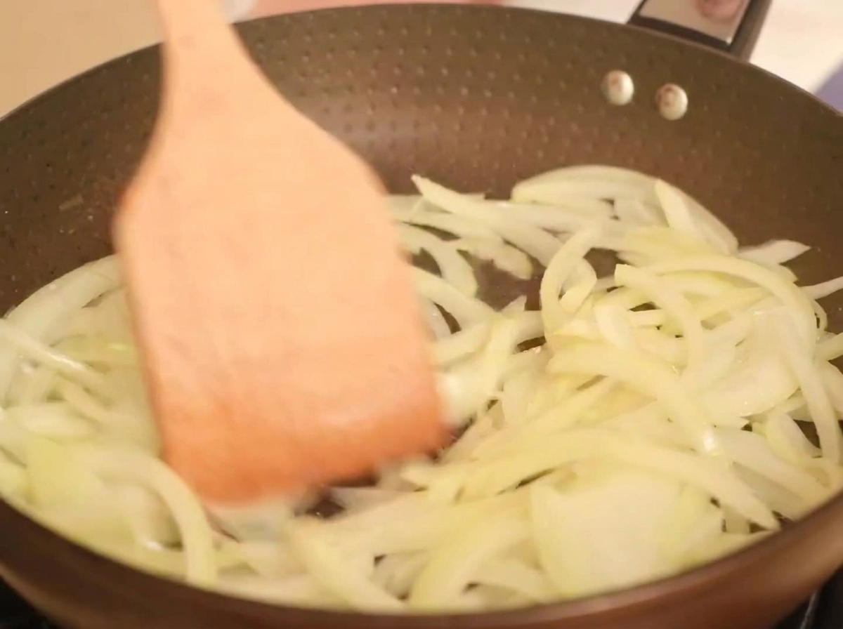 Tiras de cebolla cocinándose en una sartén caliente con aceite.