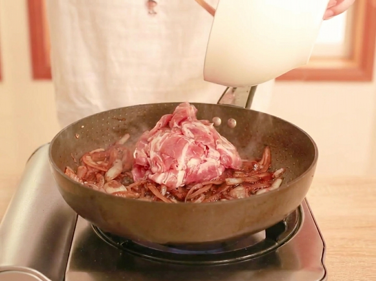 Ternera cruda en tiras siendo añadida a la sartén con la salsa.