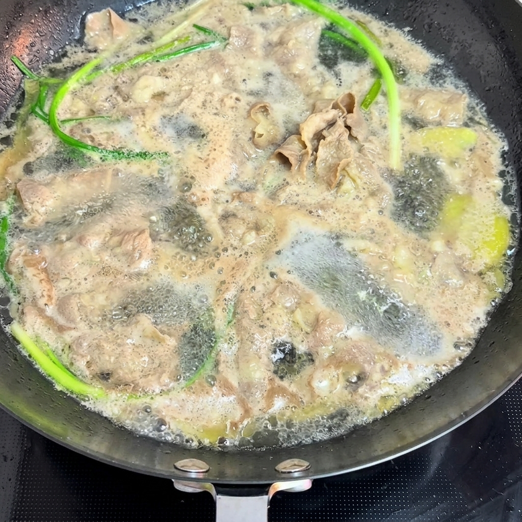 Finas láminas de carne y cebolleta escaldándose en agua hirviendo.