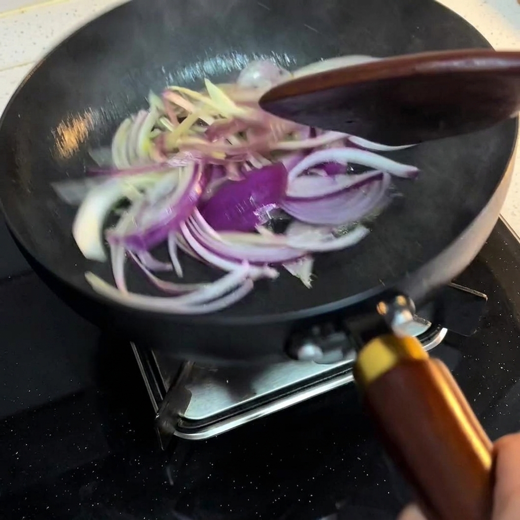 Tiras de cebolla removiéndose en una sartén con una espátula de madera a fuego medio.