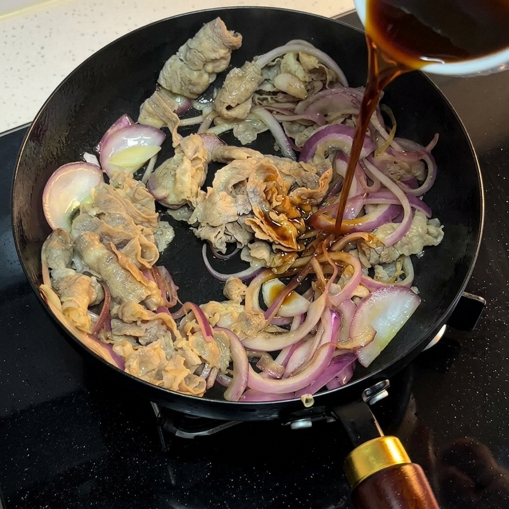 Una salsa oscura vertiéndose en la sartén con la carne dorada y la cebolla.