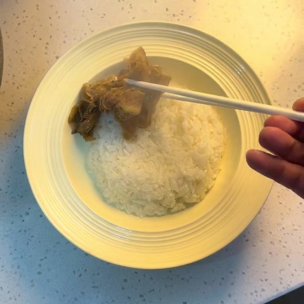 Unos palillos colocando la carne y la cebolla sobre un tazón de arroz blanco.