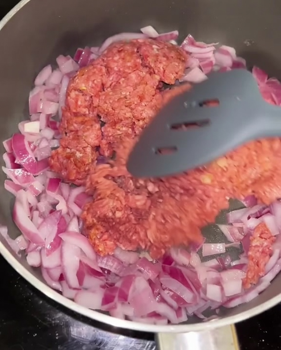 Carne picada siendo salteada con cebolla roja en una sartén.