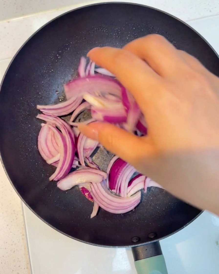 Rodajas de cebolla morada ablandándose en una sartén caliente.