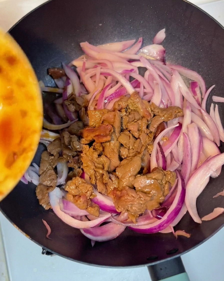 La carne cocinada mezclándose con la cebolla morada en la sartén.