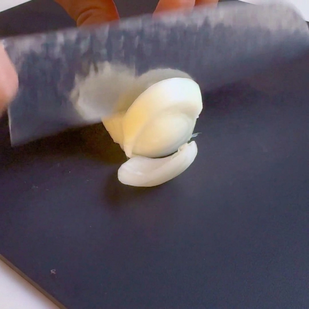 Un cuchillo cortando una cebolla blanca en tiras sobre una tabla de cortar negra.