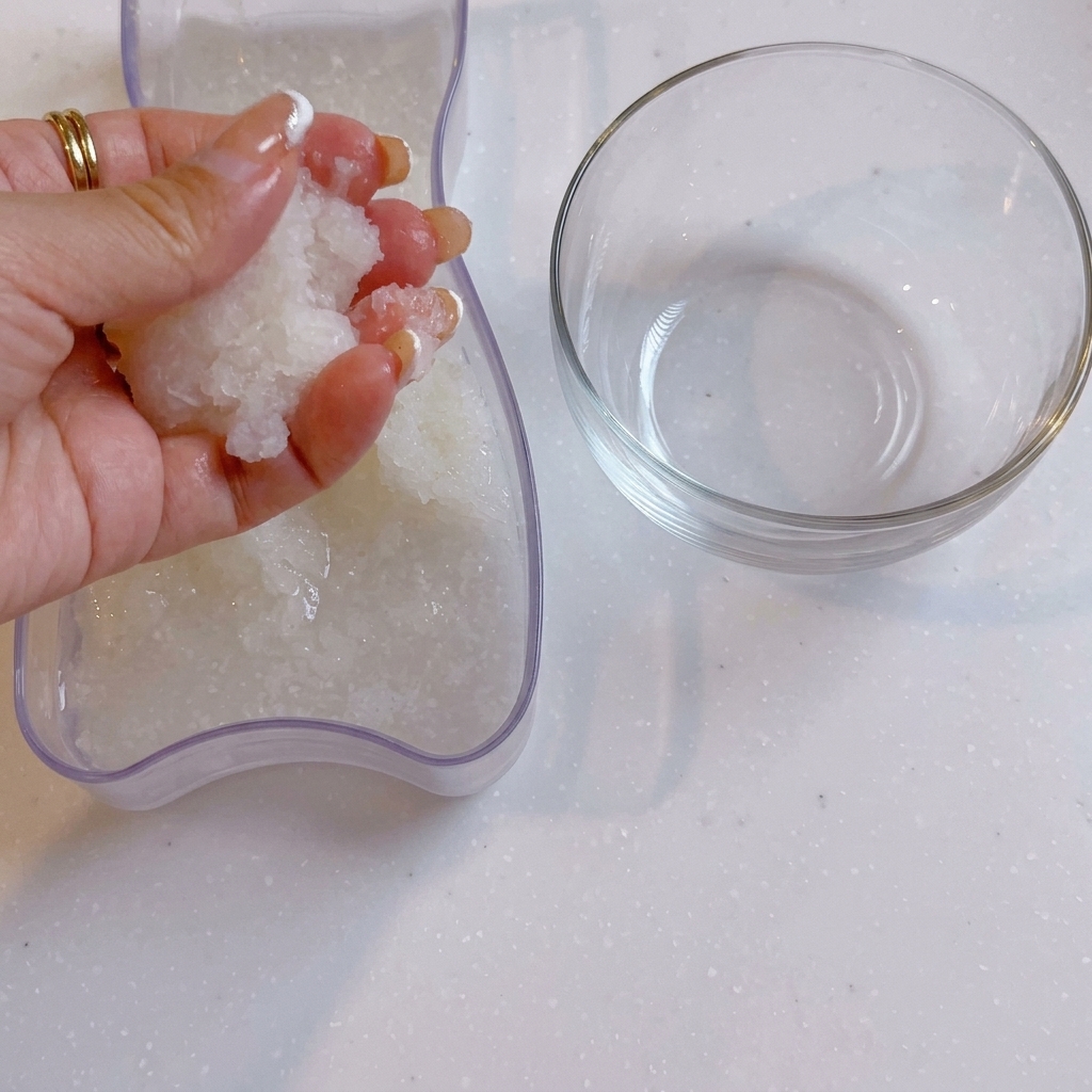 Una mano escurriendo el agua del rábano daikon rallado junto a un cuenco de cristal transparente.