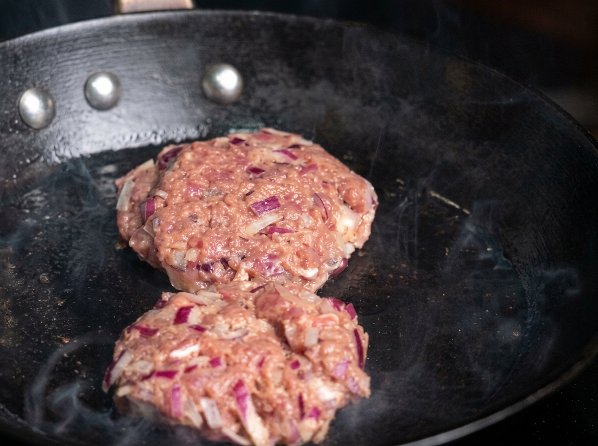 Dos hamburguesas crudas colocándose en una sartén caliente con aceite.