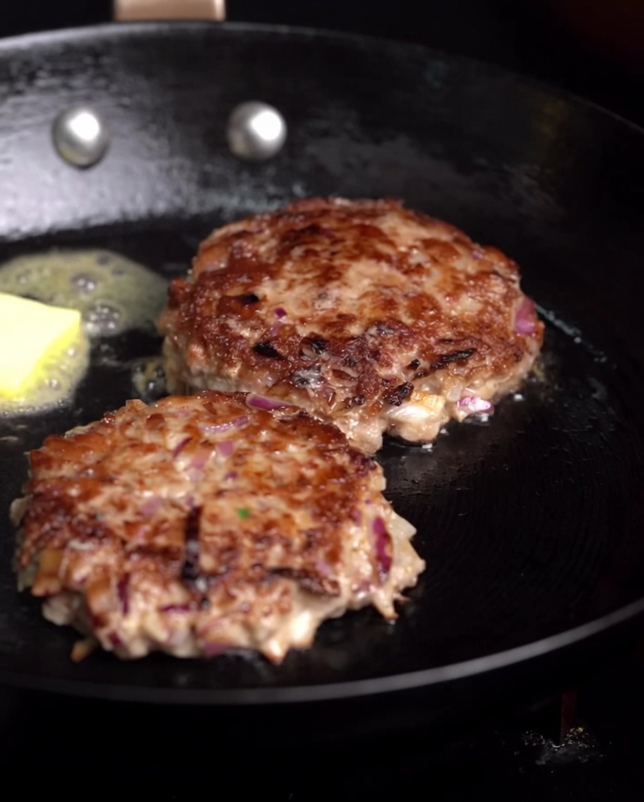 Hamburguesas friéndose con un cubo de mantequilla derritiéndose y una rama de romero.