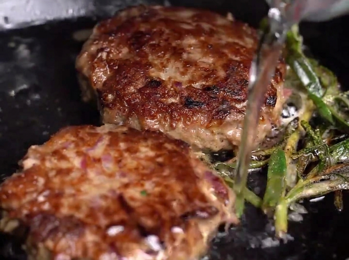 Agua vertiéndose en una sartén con hamburguesas, creando vapor.