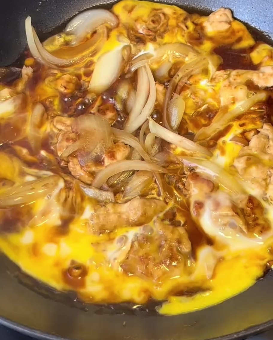 Cebollas cortadas siendo salteadas con pollo dorado en una sartén.