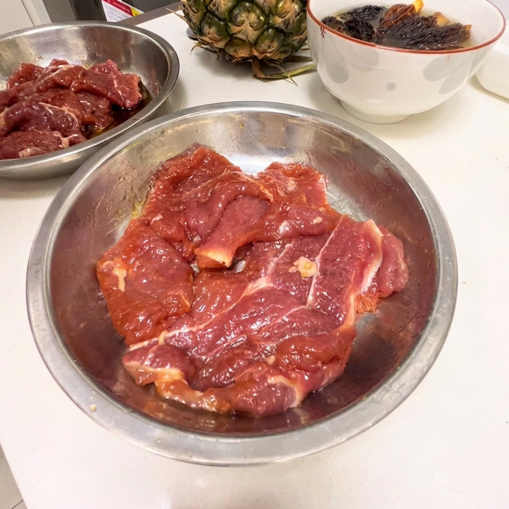 Finas rodajas de paleta de cerdo cruda en un bol de acero inoxidable con adobo oscuro.