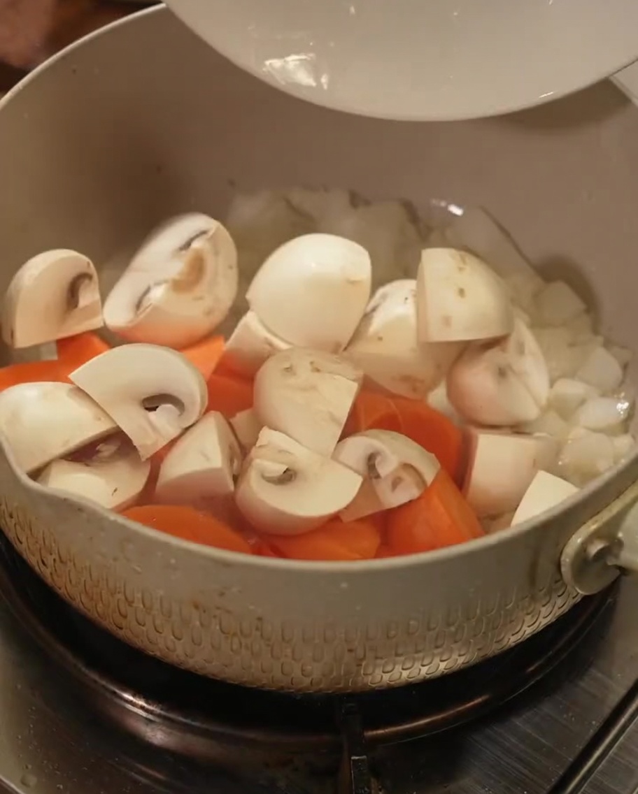 Trozos de zanahoria fresca y rodajas de champiñón mezclándose en una olla.
