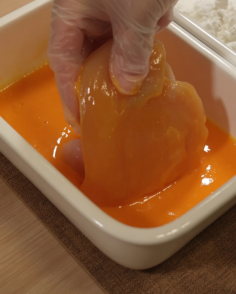 Pechuga de pollo sumergiéndose en una mezcla amarilla de huevo batido.