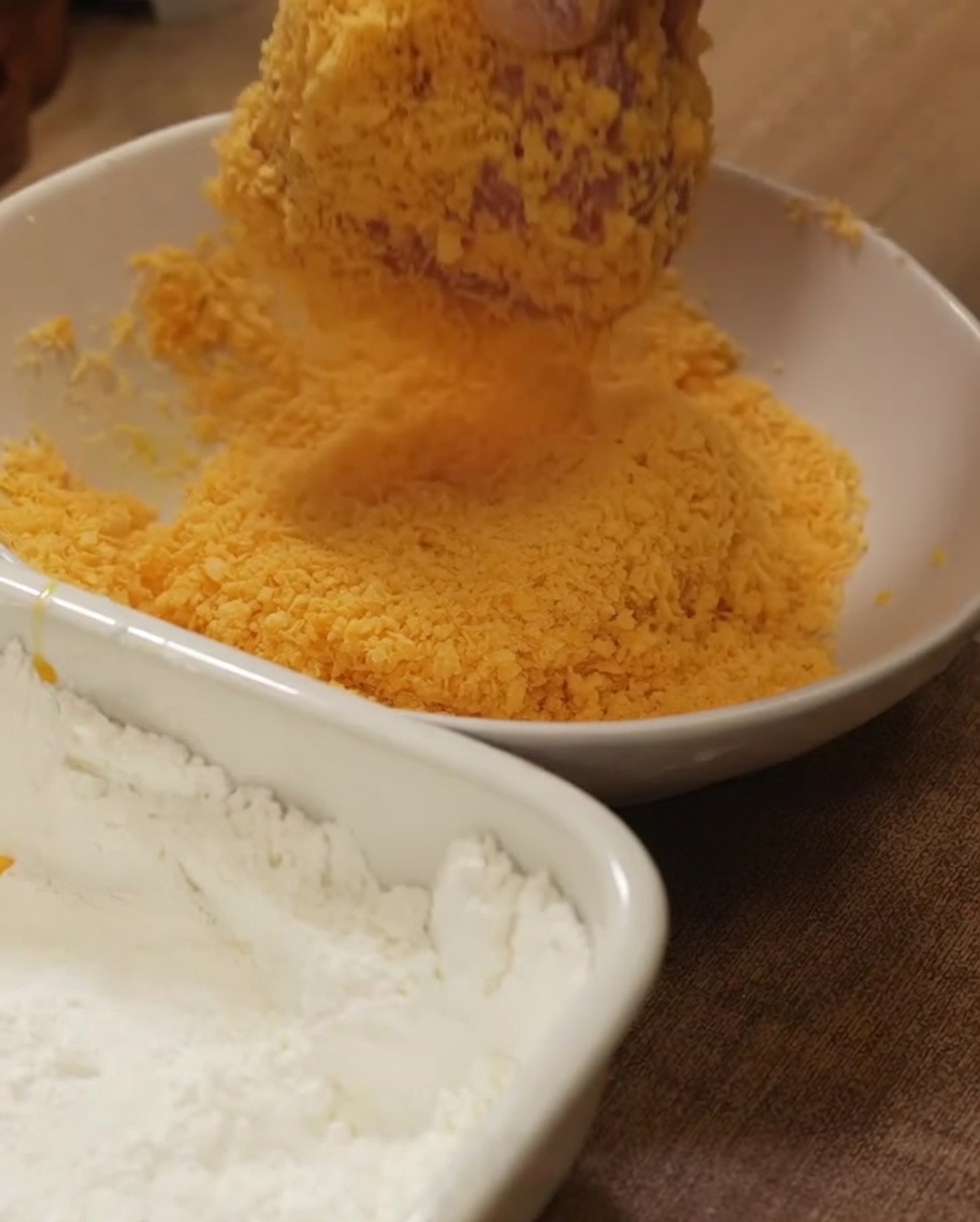 Pechuga de pollo presionada firmemente en un bol de pan rallado dorado para obtener una capa uniforme.
