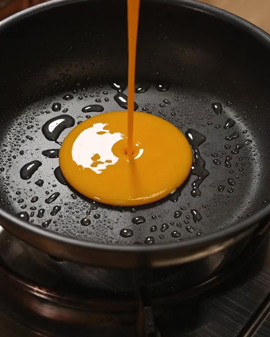 Mezcla dorada de huevo siendo removida en una sartén antiadherente para crear huevos revueltos ligeros y esponjosos.