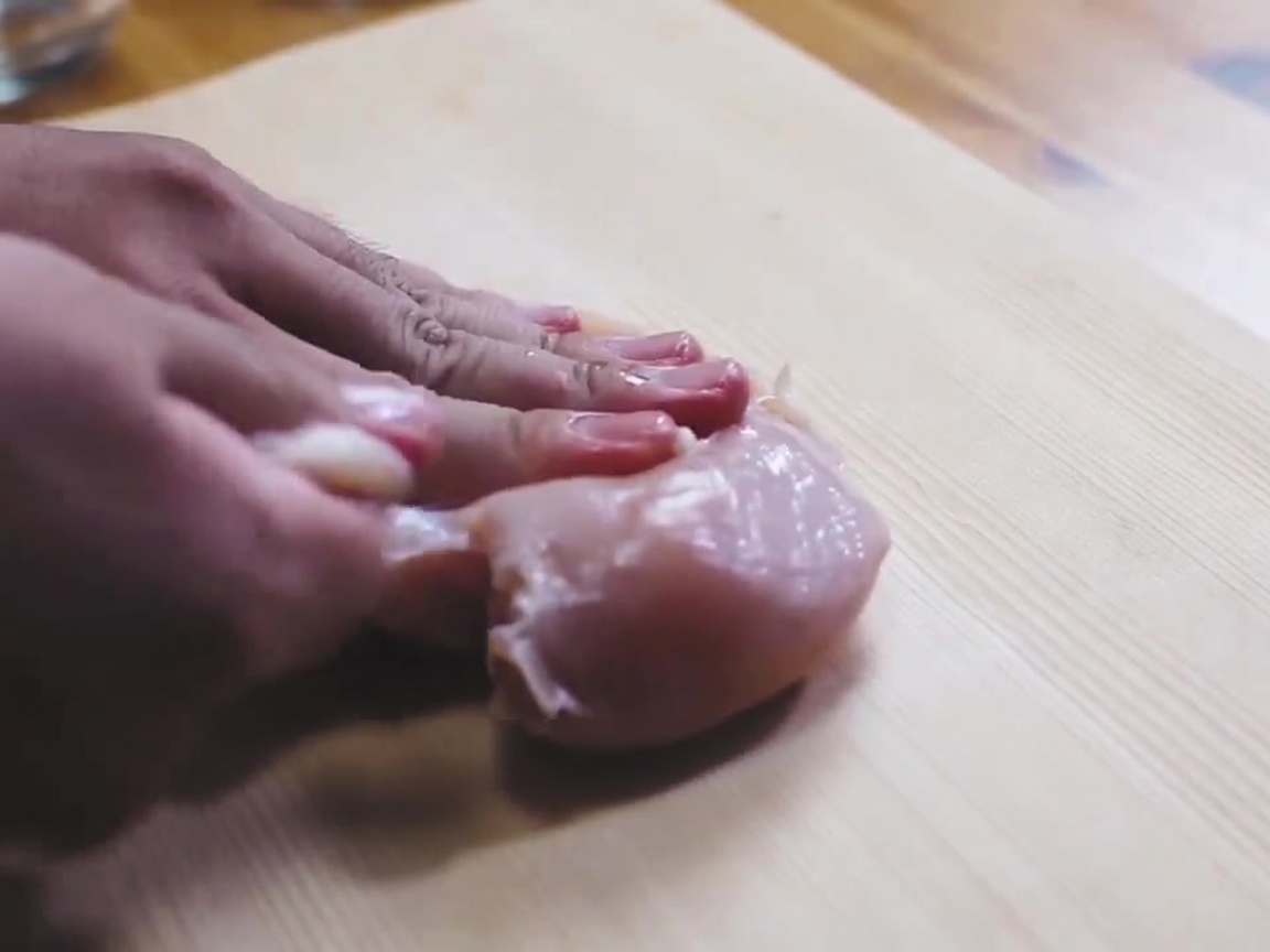 Una pechuga de pollo cruda espolvoreada con sal sobre una tabla de cortar de madera.