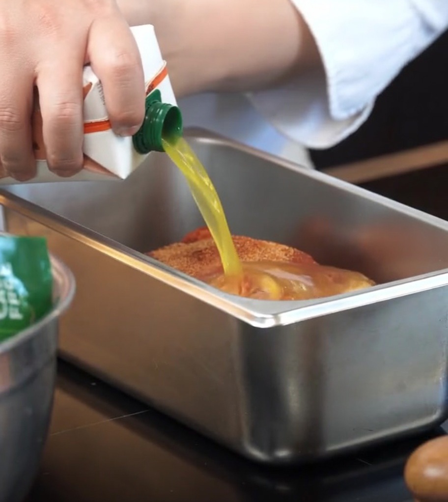 Jugo de naranja vertido desde un envase a la bandeja con el cerdo sazonado.