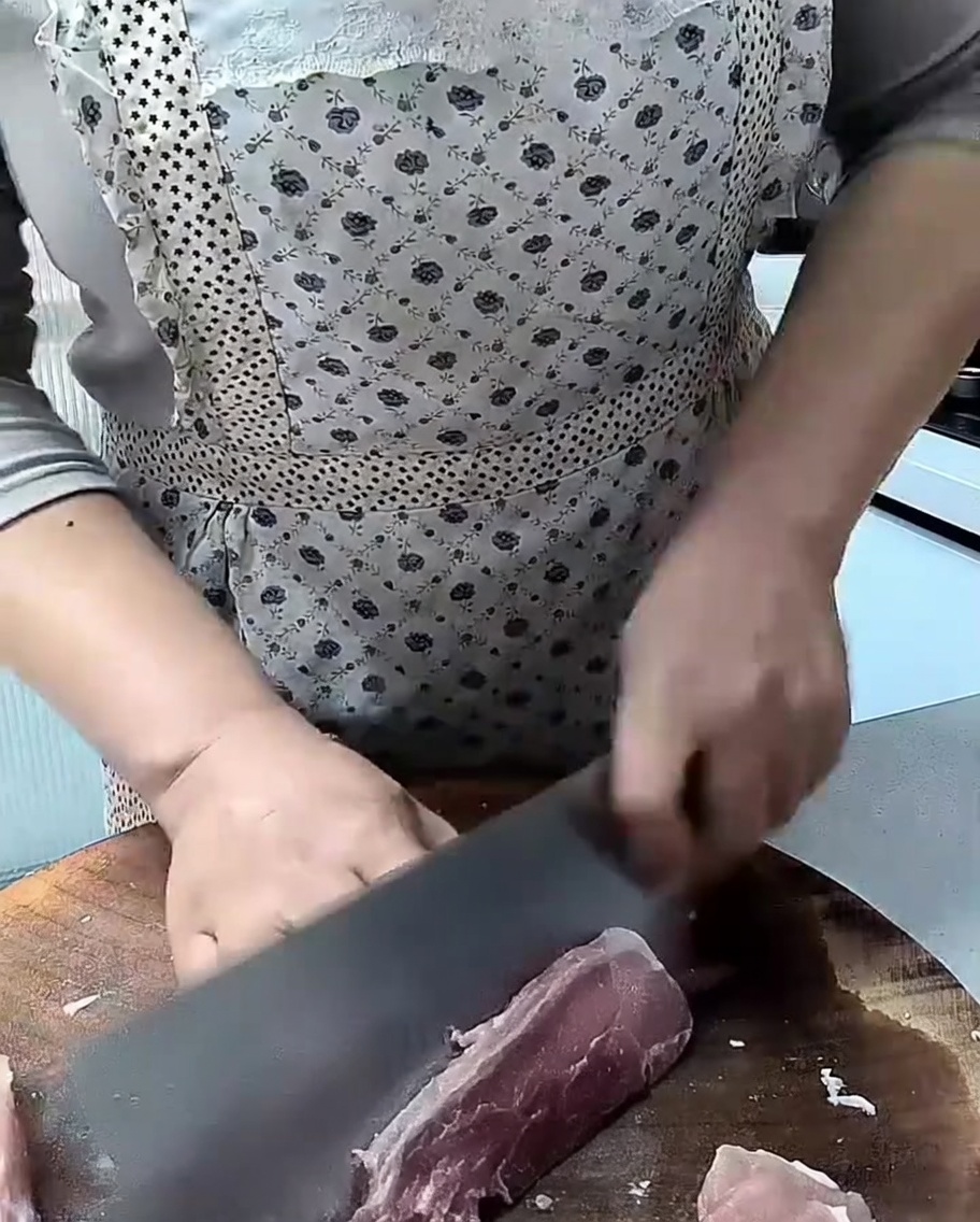 Un cuchillo afilado cortando trozos de lomo de cerdo crudo sobre una tabla de madera.