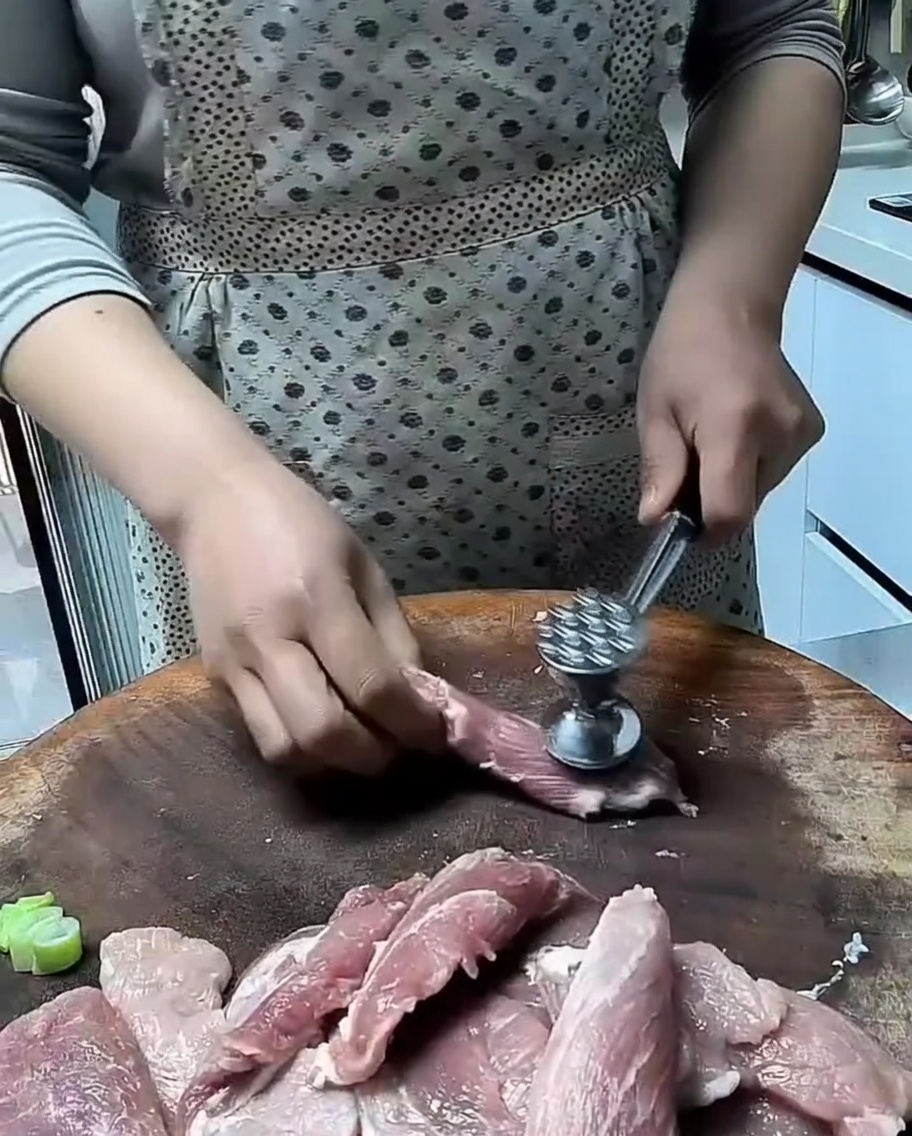 Un mazo de cocina ablandando lonchas de cerdo sobre una superficie de madera.