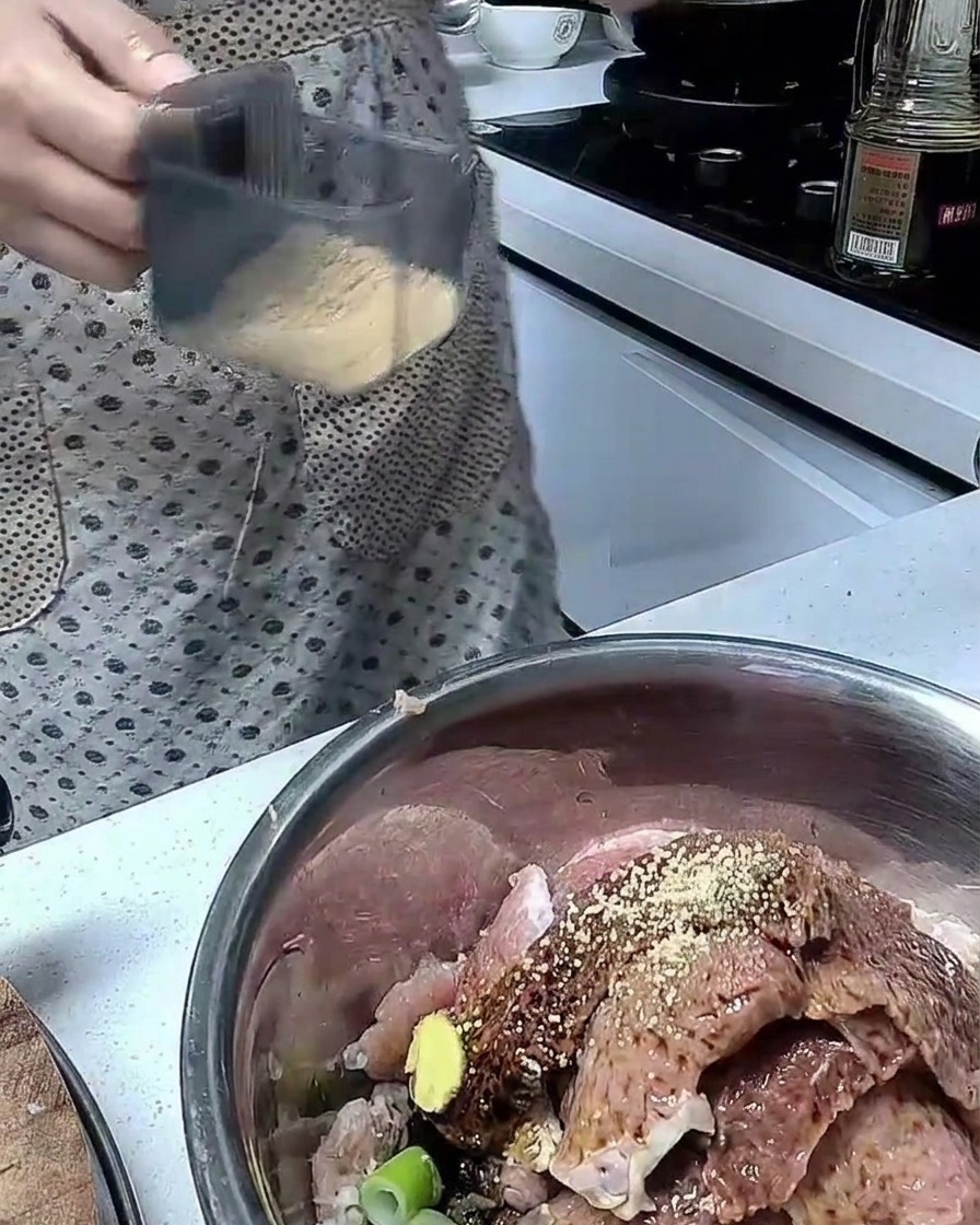 Ingredientes mezclándose con trozos de cerdo crudo en un bol de acero inoxidable.