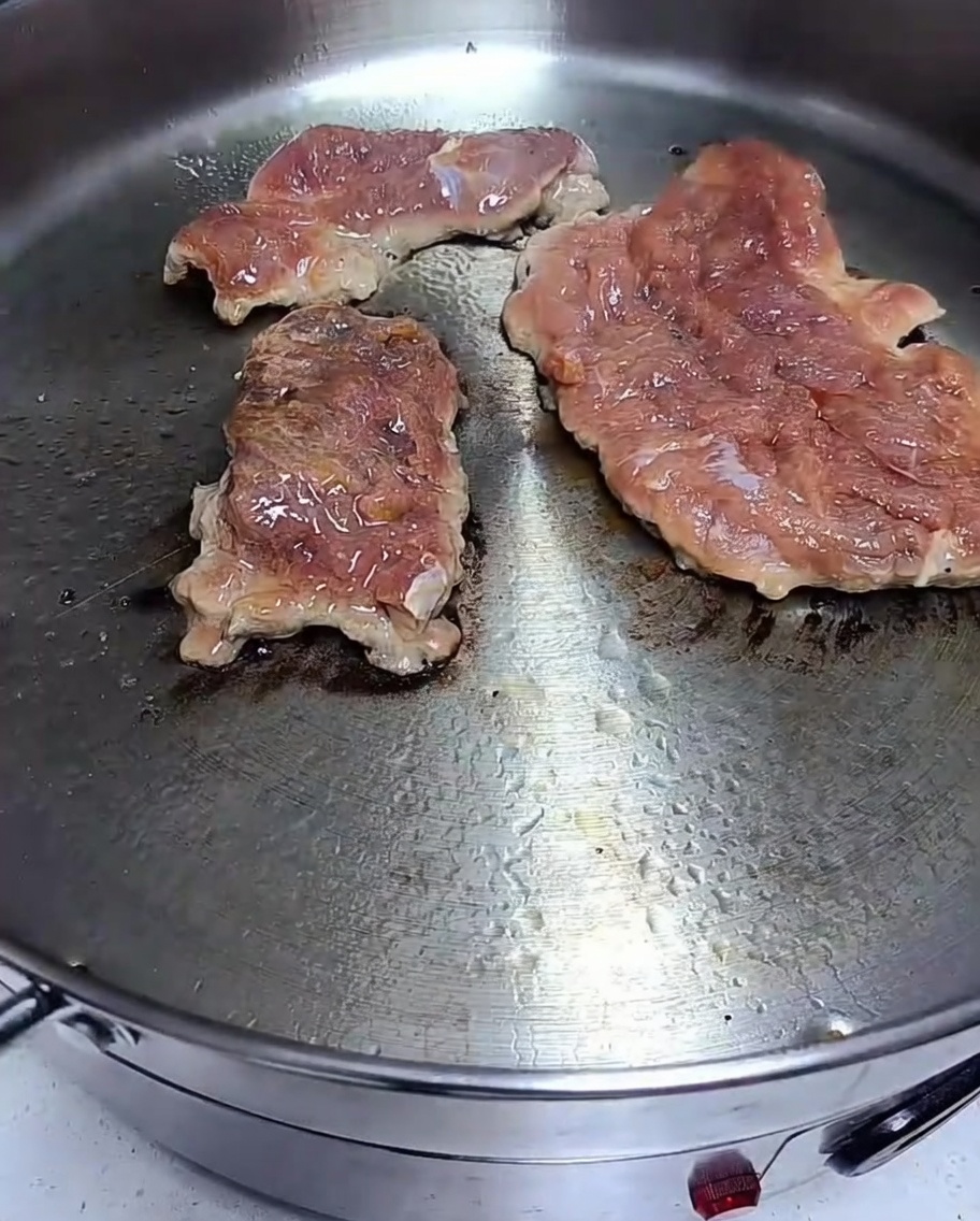 Chuletas de cerdo marinadas sellándose en una sartén caliente con dorado visible.