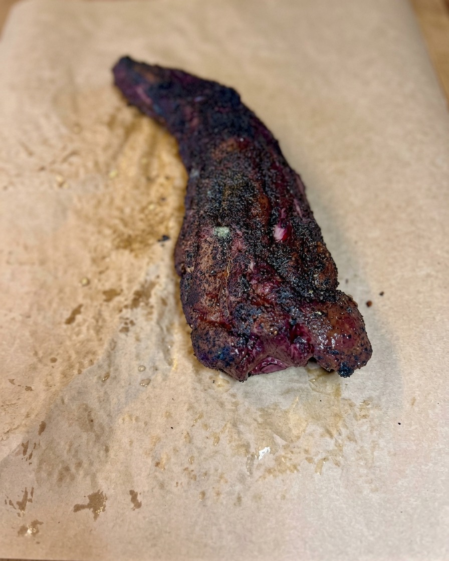 Una costilla de res ahumada siendo enrollada firmemente en papel de estraza para formar un paquete completo.