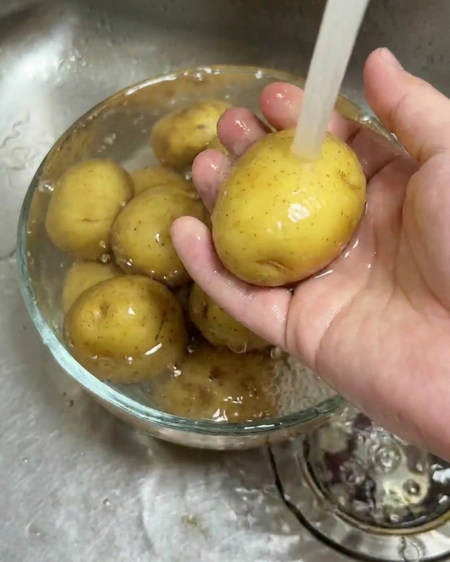 Patatas baby limpiándose en un bol de cristal bajo un chorro de agua corriente.