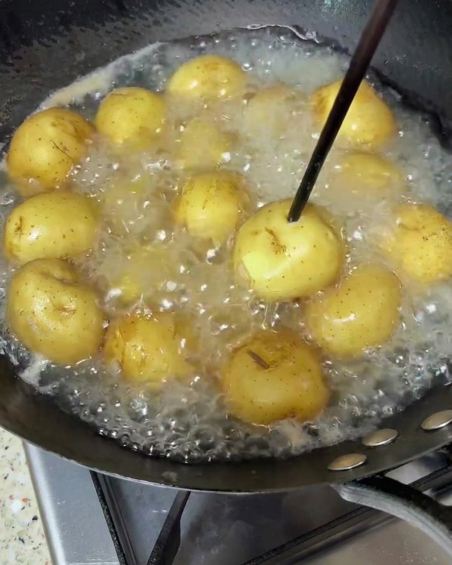 Patatas baby cociéndose a fuego lento en agua hirviendo, comprobando su punto con un palillo de madera.