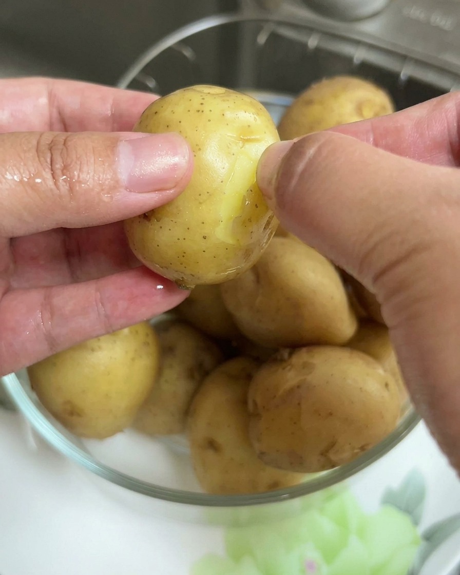 Primer plano de unas manos retirando la fina piel de una patata baby hervida.