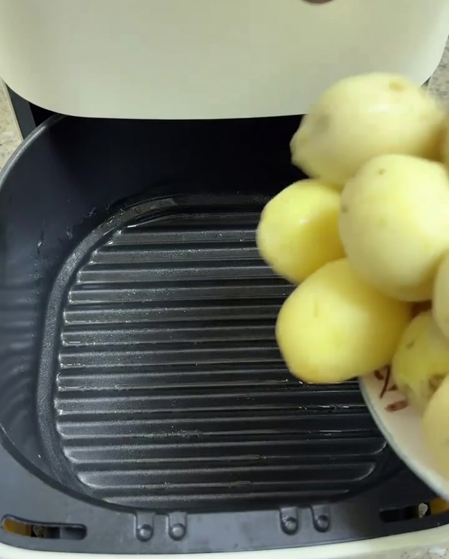 Patatas baby peladas colocándose en la cesta de la freidora de aire.