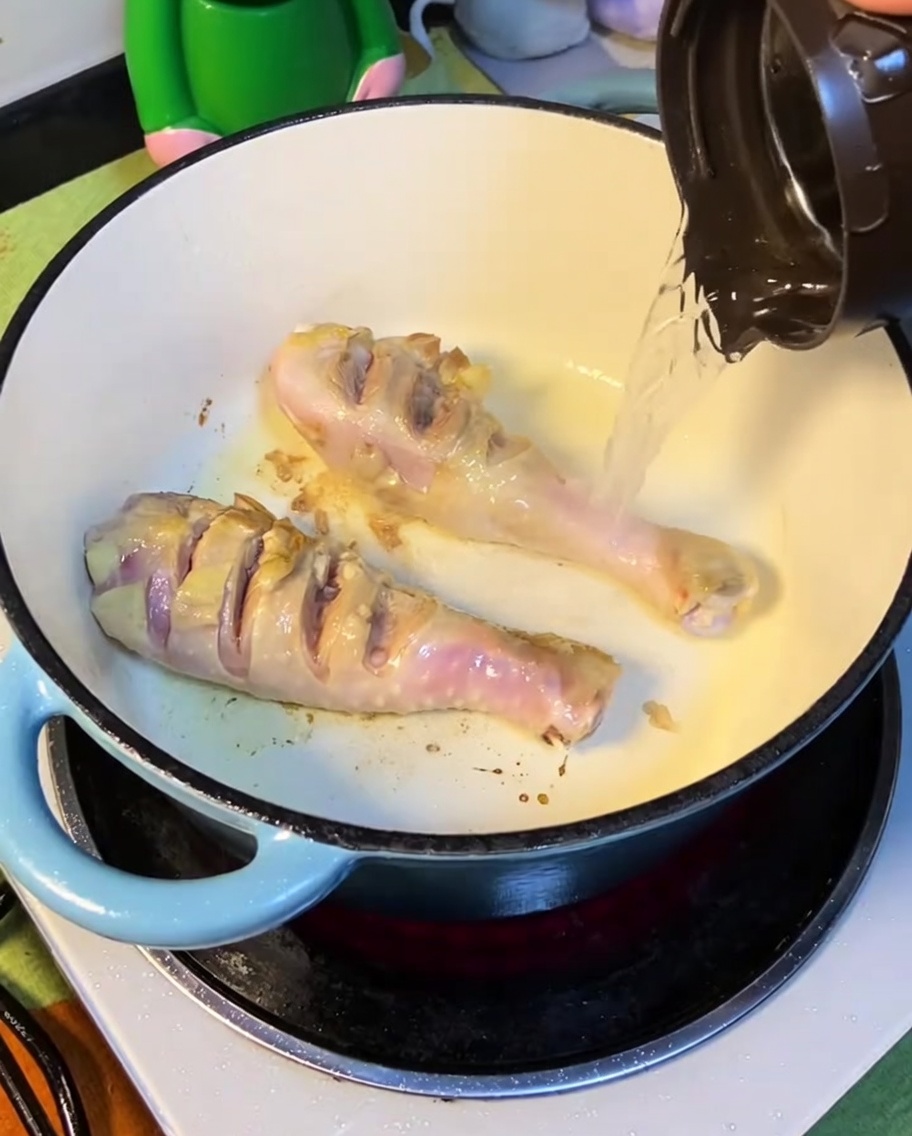 Agua hirviendo vertiéndose en la olla con el pollo sellado.