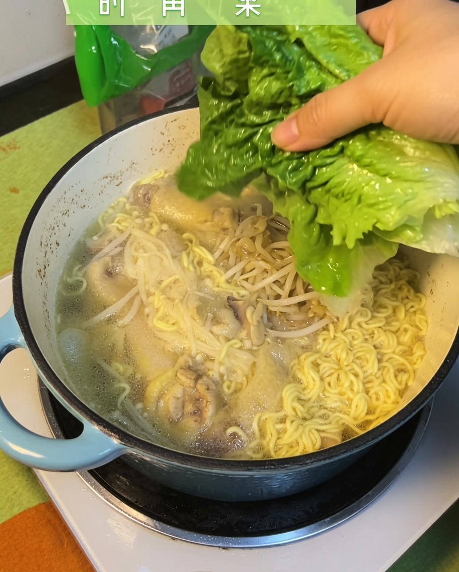 Hojas frescas de bok choy verde siendo añadidas a la sopa de pollo y fideos terminada.