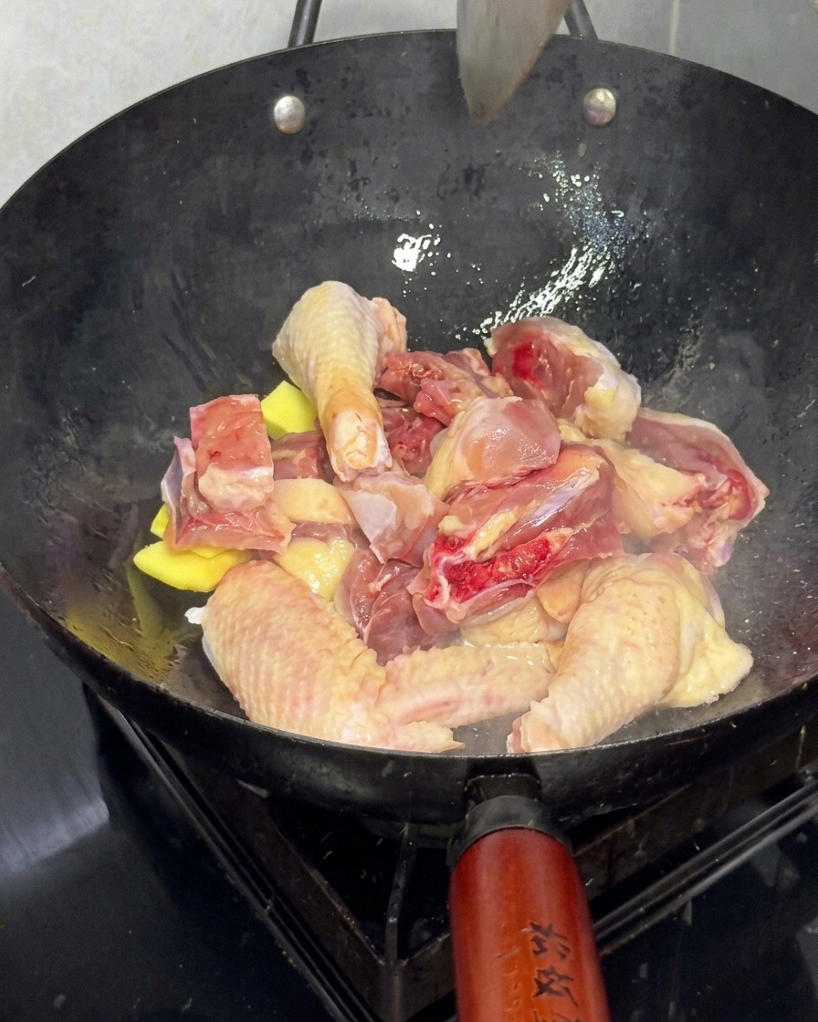 Trozos de pollo fresco salteándose con rodajas de jengibre en un wok grande.