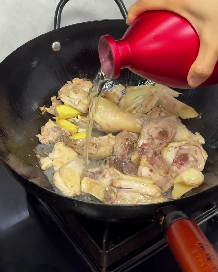 Vertiendo vino de arroz sobre los trozos de pollo en un wok durante el proceso de salteado.