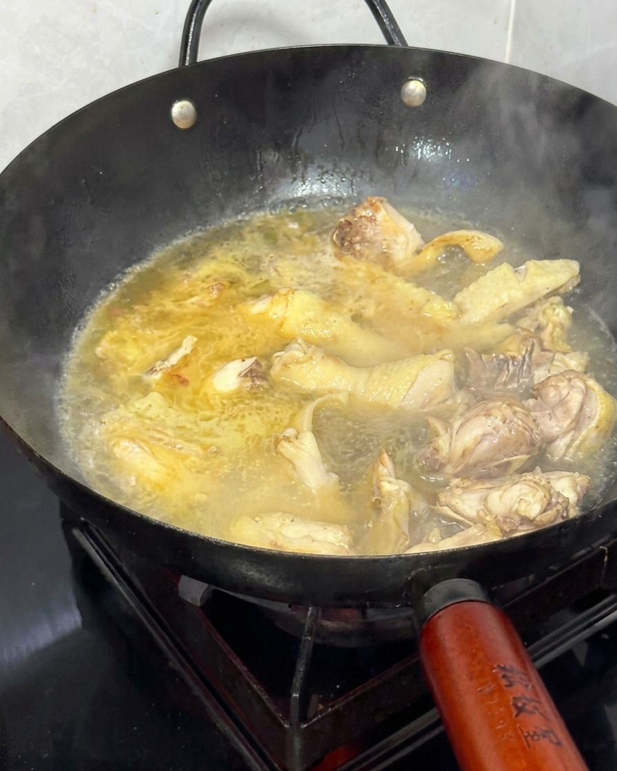 Añadiendo agua caliente a un wok lleno de pollo salteado y jengibre.