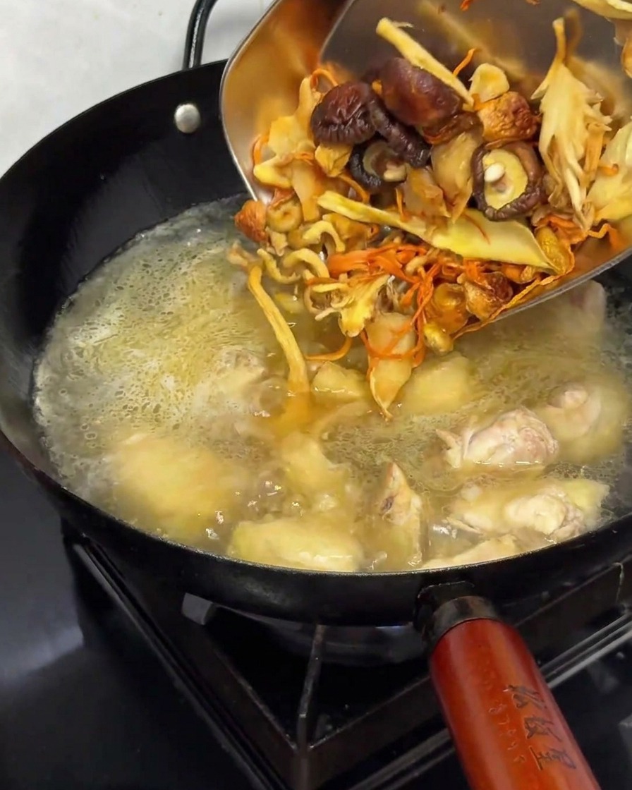 Añadiendo setas deshidratadas rehidratadas a una olla con pollo y caldo.