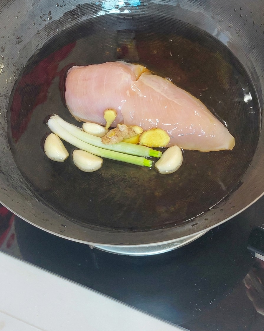 Pechuga de pollo cocida siendo levantada de un wok con una espumadera y palillos.