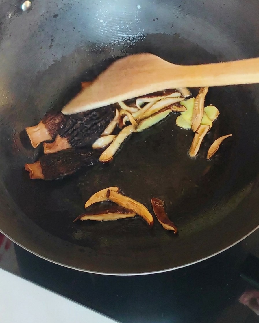 Pollo desmenuzado mezclado con setas y jengibre en un wok.
