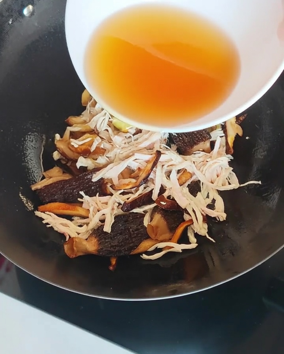 Un líquido de remojo de setas claro y color ámbar siendo vertido en un wok con pollo y setas.