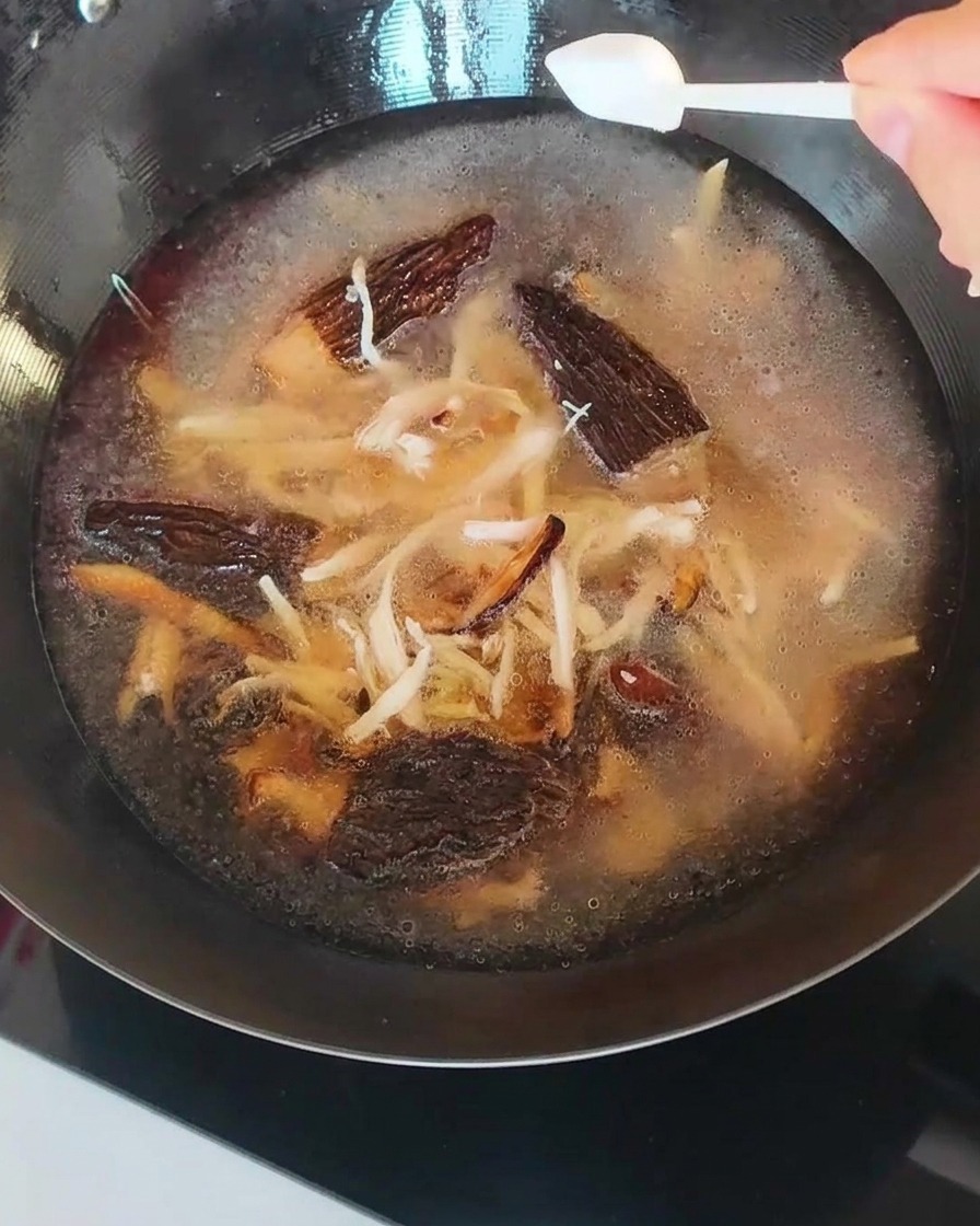 El caldo en el wok, con setas y pollo desmenuzado, siendo sazonado con una cucharadita de sal.