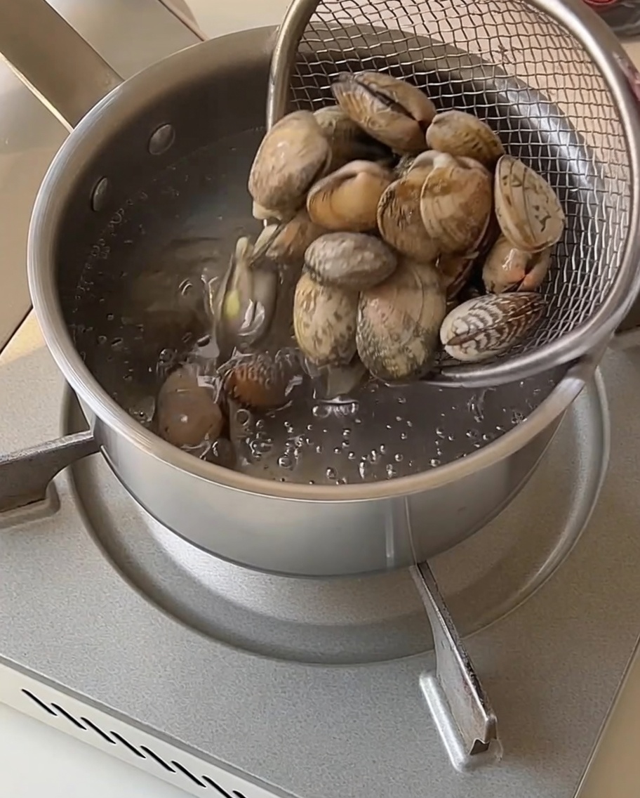 Almejas en un colador de malla siendo retiradas de una olla con agua hirviendo.