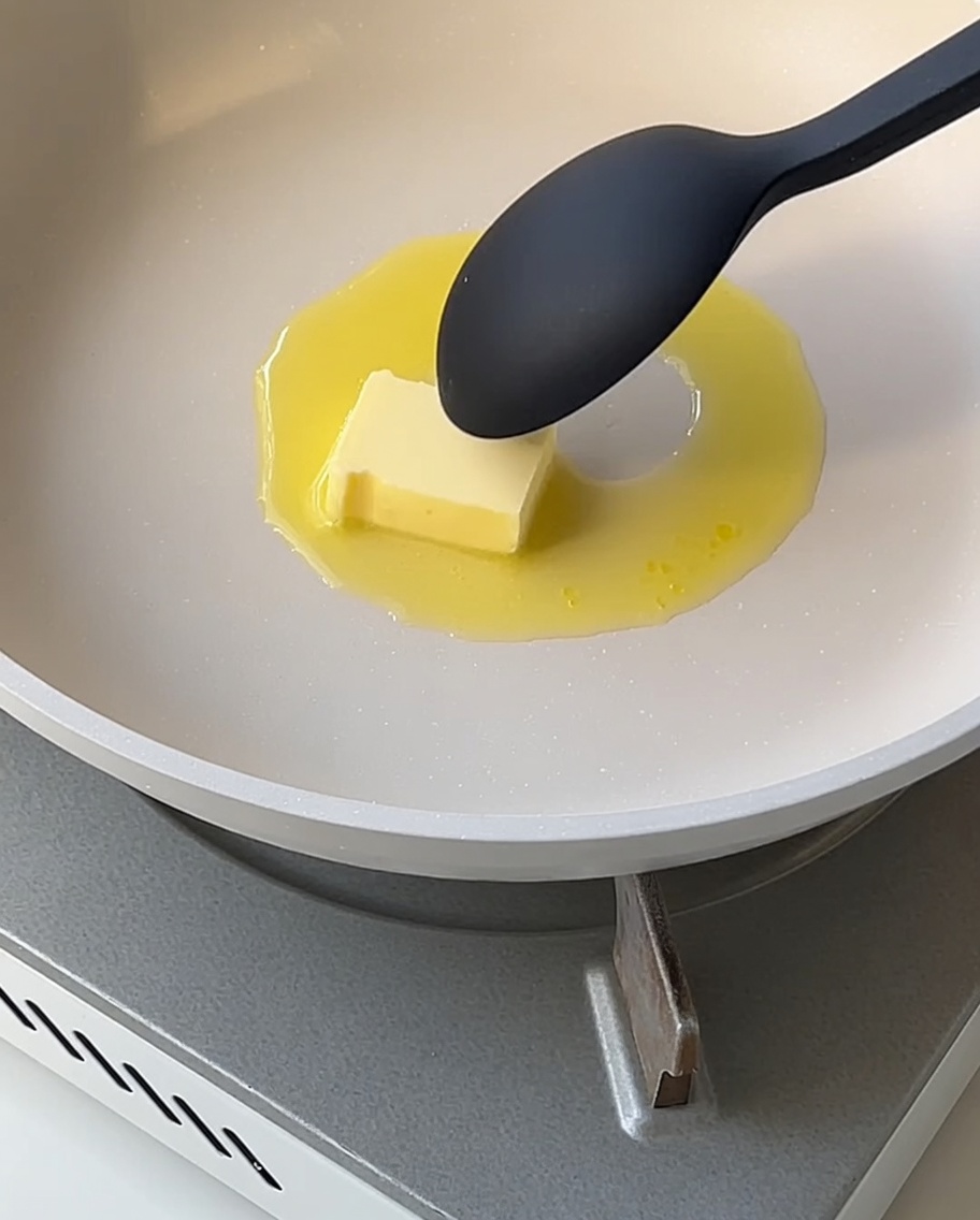 Una salsa blanca suave espesándose en una sartén mientras se remueve con una cuchara.