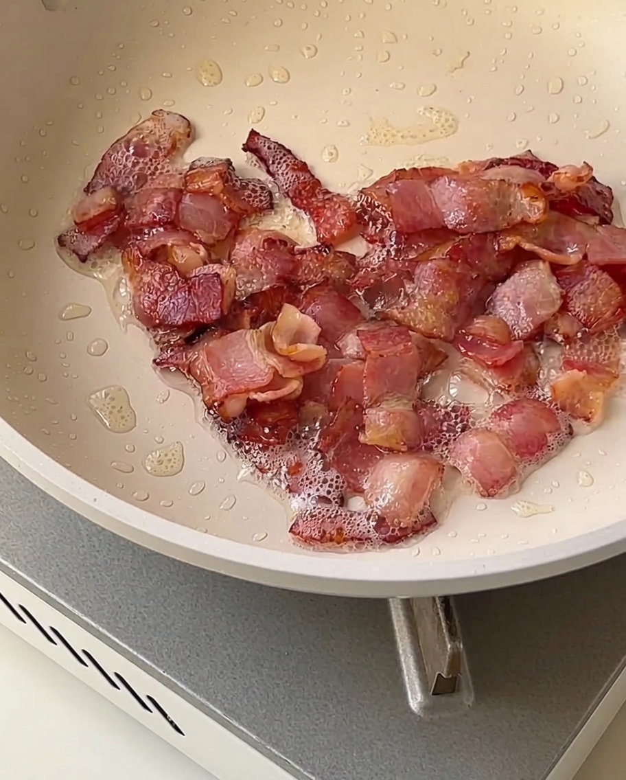 Cubitos de cebolla, apio y papa friéndose en una sartén con trozos de tocino crujiente y dorado.
